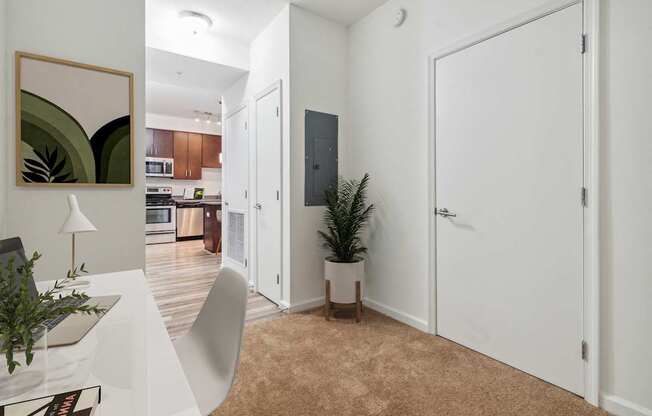 a room with a desk and a door to a kitchen and a living room