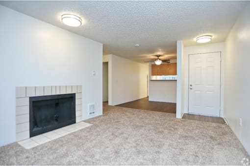 an empty living room with a fireplace and a kitchen