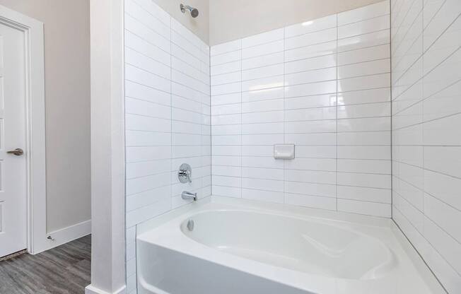 A white tiled bathroom with a white bathtub and a white door.