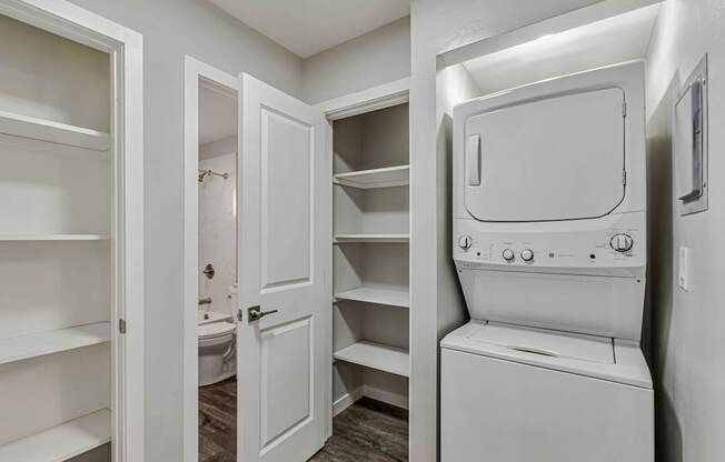 A white washer/dryer and shelves in a small closet.