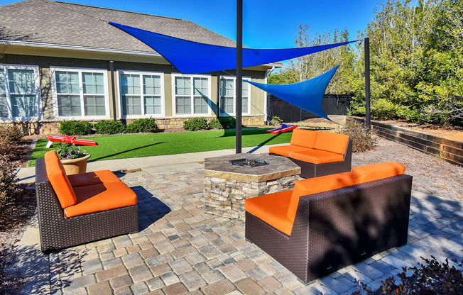 a patio with a fire pit and lounge chairs in front of a house