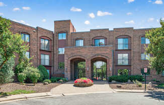 A red brick building with a large arched entrance and a small garden in front.