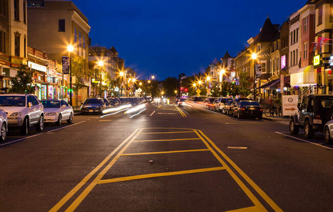 A city street at night with cars parked on the side.
