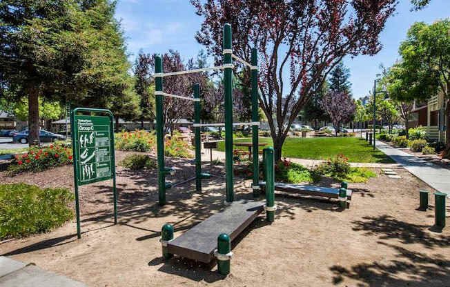 A green outdoor gym with a sign that says "Outdoor Gym" is surrounded by trees and bushes.