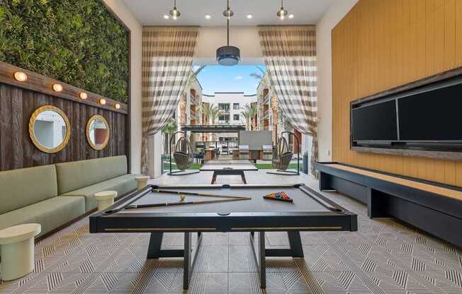 A billiard table is in the middle of a room with a green wall on the left and a television on the right.