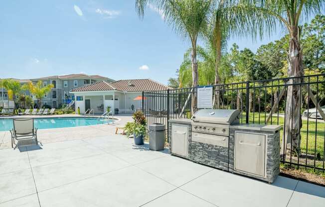 Grill with a palm tree and pool in the background at Trillium apartments in Melbourne fl