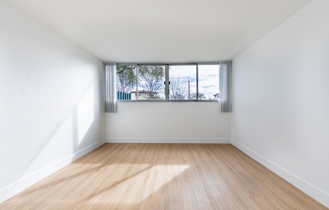 an empty room with wooden floors and a window at Avenue Two Apartments, Redwood City  , CA