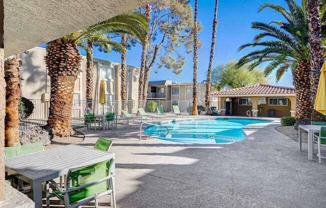 A pool area with a table and chairs and palm trees.