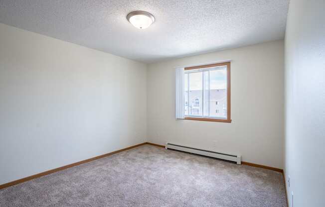 A room with a window and a carpeted floor. Bismarck, ND Sierra Ridge Apartments
