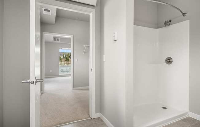 a bathroom with a shower and a door to a room with a hallway and a