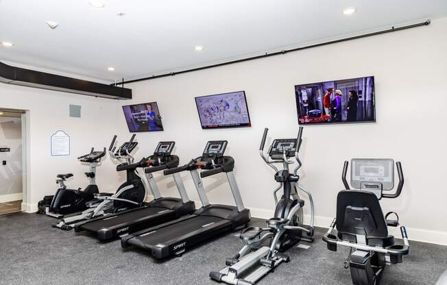 a gym with cardio machines and televisions on the wall