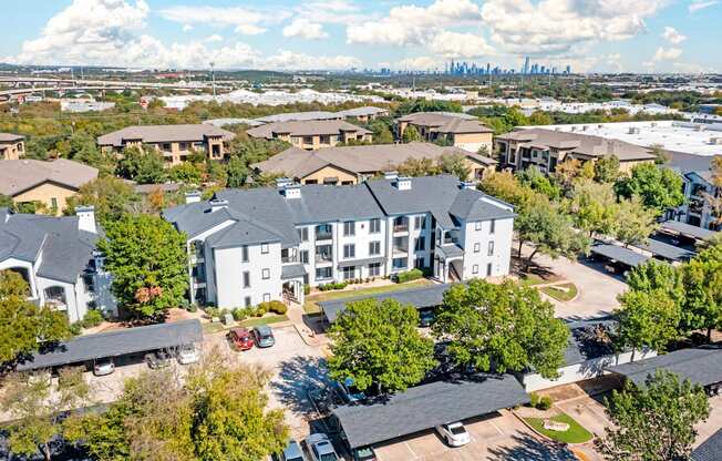 A large white building is surrounded by smaller buildings and trees.
