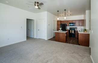 an empty living room with a kitchen and a ceiling fan