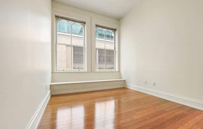 an empty bedroom or office with large windows and hard wood floors