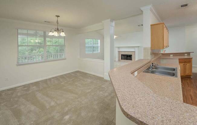 A large, empty living room with a fireplace and a kitchen area in the background.