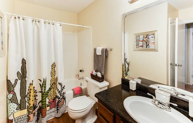 a bathroom with a white toilet next to a sink with a shower curtain with a cactus