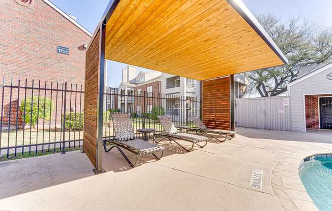 A wooden covered patio area with a pool and lounge chairs.
