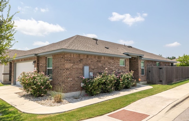 a brick house with green shutters and pink flowers in the front yard