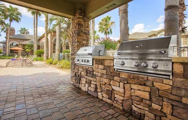 a barbecue grill on a stone wall in a backyard with palm trees