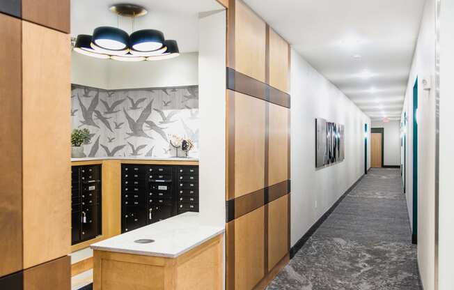 Interior view of a modern apartment complex mail room featuring rows of individual mailboxes neatly arranged along the wall. In the center, there is a flat-screen TV displaying important community announcements and updates.