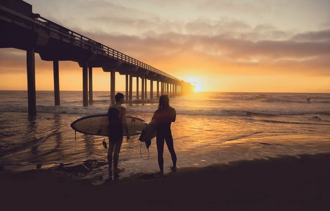 two people standing on the beach with surfboards at sunset