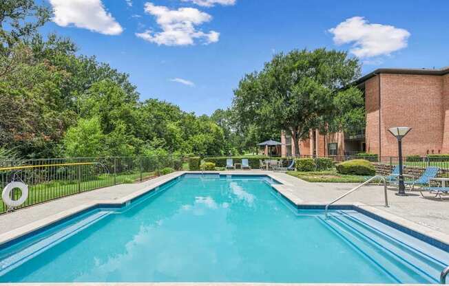 A swimming pool surrounded by trees and a building in the background.