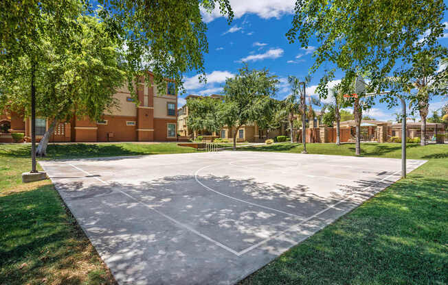 A basketball court is surrounded by trees and a building in the background.