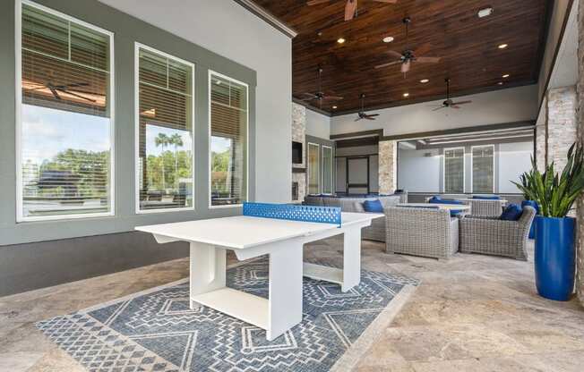 A white dining table is surrounded by grey wicker chairs in a room with a wooden ceiling.