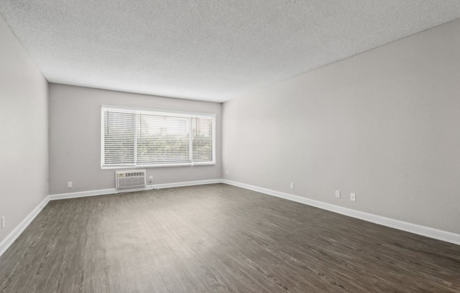 an empty living room with wood floors and a window