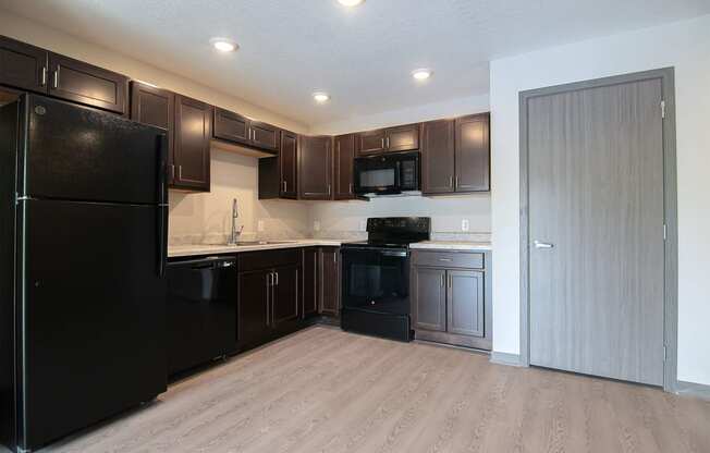 an empty kitchen with black appliances and dark wood cabinets