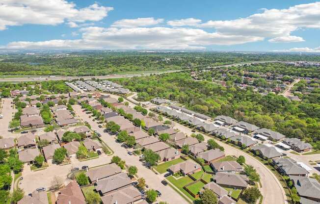 A suburban neighborhood with houses and greenery under a blue sky.