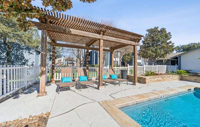 A pool area with a wooden pergola and lounge chairs.