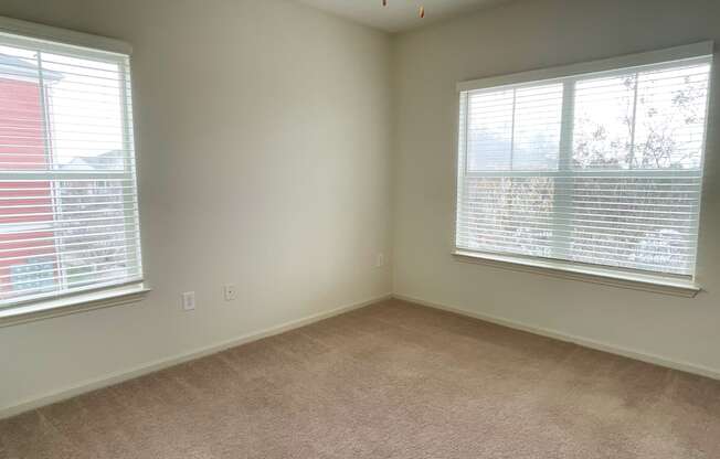 an empty living room with two windows and carpet
