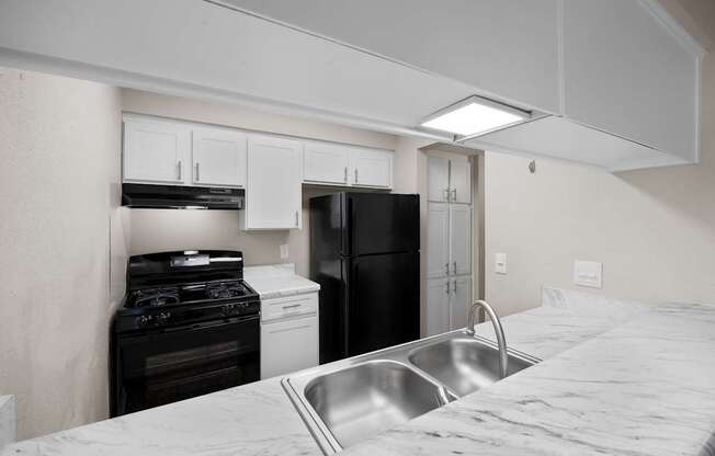 A kitchen with a black refrigerator, white oven, and a stainless steel sink.