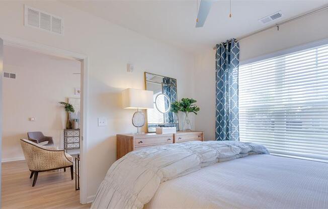 Spacious furnished bedroom with 9ft ceilings, window with ample natural lighting, and view of dining area at The Station at Savannah Quarters apartments for rent