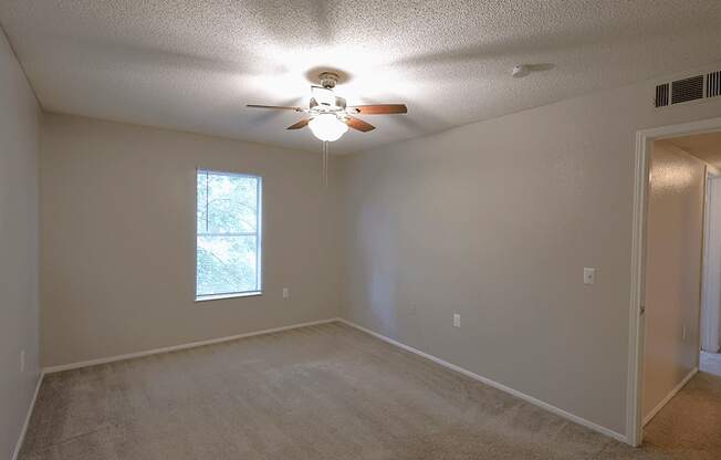 an empty living room with a ceiling fan and a window