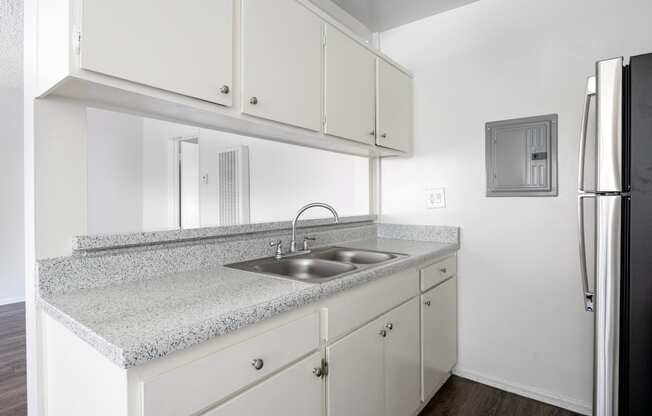 an empty kitchen with white cabinets and a sink and refrigerator