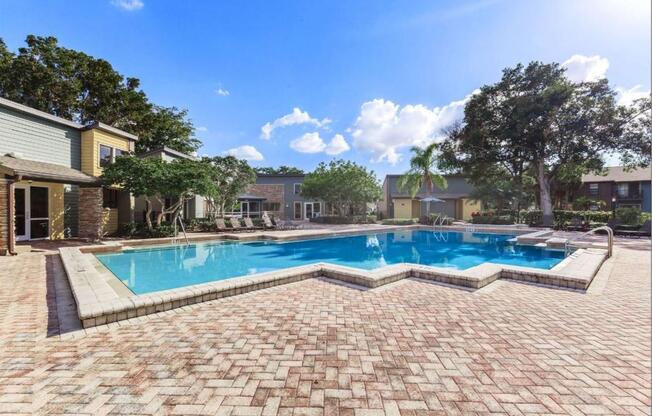 a large swimming pool with a patio and buildings in the background