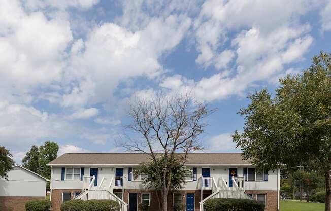 A white house with a blue door and a tree in front.