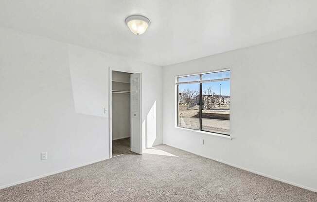 A bedroom with a carpeted floor, a large window, and a closet at Trappers Cove Apartments, Lansing