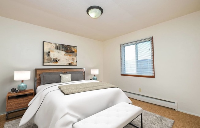 a bedroom with a white bed and a white couch. Fargo, ND North Manor Apartments