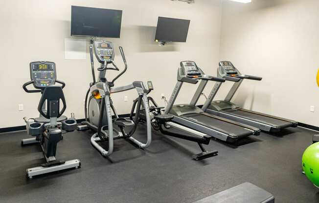 a gym with four ellipticals and a tv on the wall