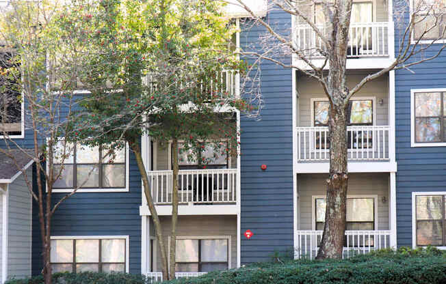 the exterior of a blue apartment building with trees and shrubs