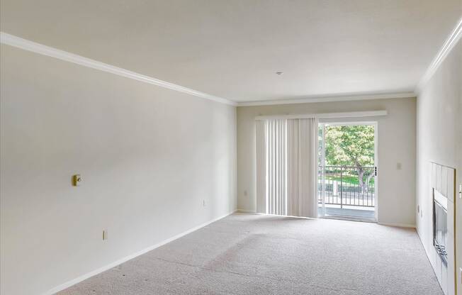 A large, empty room with a carpeted floor and a sliding glass door leading to a balcony.