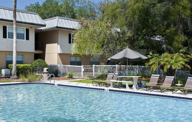 a swimming pool with chairs and a umbrella in front of a house