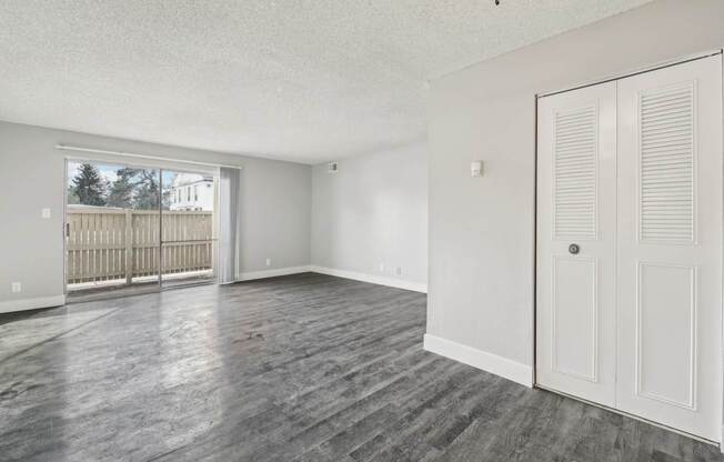 A room with a white door and a window with a view of a fence and a building outside.