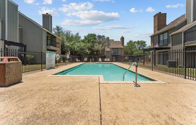 A swimming pool surrounded by a fence and a sandy area.