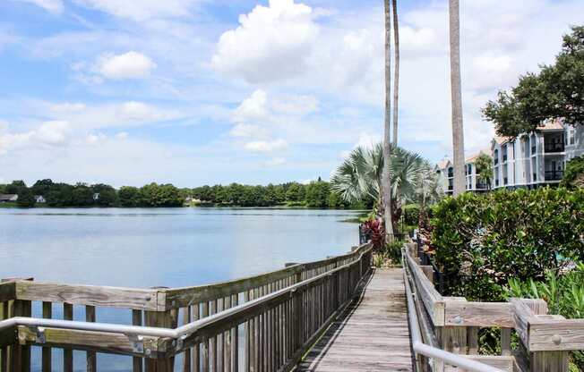 A wooden walkway leads to a body of water with a house on the right.
