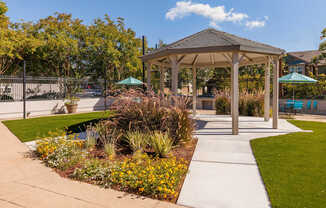 A gazebo is surrounded by a garden with a pond and a fence.