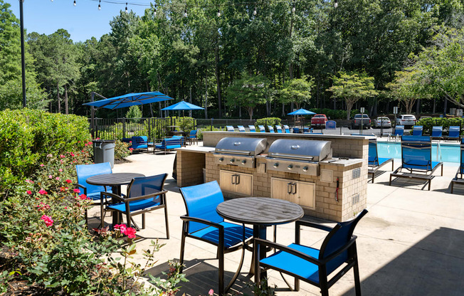 A patio with blue chairs and tables is surrounded by greenery.